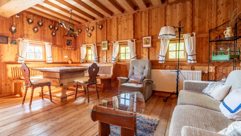 Wohn- und Essbereich, © Wiener Alpen / Christian Kremsl Rustikaler Wohn- und Essbereich mit Holzmöbeln, Holzwänden und Jagdtrophäen an der Wand.