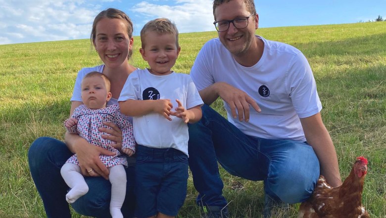 Familie Stangl, © Stangl Eine Familie mit zwei Kindern und mit einem Huhn auf einem Feld unter blauem Himmel.