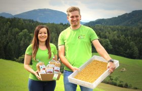 Aus der Nudelwerkstatt List, © Familie List Zwei Personen in grünen T-Shirts präsentieren Nudeln vor einer Berglandschaft.