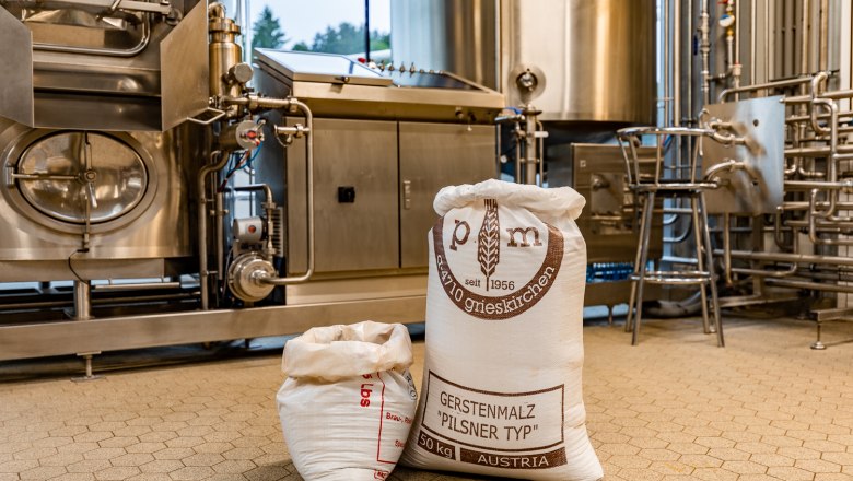 Schwarzbräu - Brauerei, © Wiener Alpen, Christian Kremsl Säcke mit Gerstenmalz in einer Brauerei vor Edelstahlmaschinen.