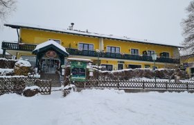 Krumbacherhof, © Wiener Alpen / Cornelia Schuh Gelbes Gebäude im Schnee mit grüner Veranda und Eingang.