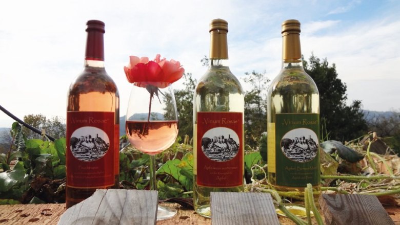 Apfelweine der Familie Winkler, © Familie Winkler Drei Flaschen Apfelwein und ein Glas mit Apfelwein und einer Rose auf einem Holzbalken im Freien.