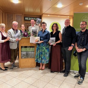 vlnr.: Petra Weber, Autor Alfred Weber, Grafikerin Anna Schiefer, Thomas Scherz, Mag. Katrin Scherz-Kogelbauer, Lektorin Elisabeth Zenz, Food-Fotograf Markus Proske, Fotograf Thomas Gobauer, © Scherz-Kogelbauer Mehrere Personen stehen vor der Rezeption im VitalZeit Hotel Weber, einige halten ein Kochbuch in der Hand.