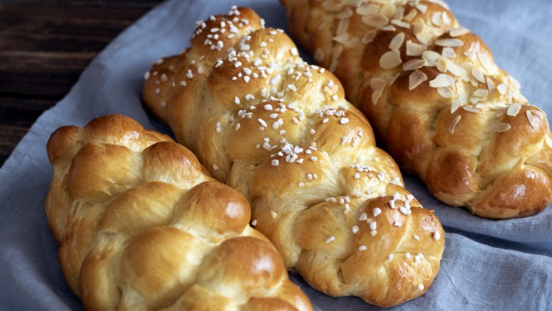 Briochstrizel, © Fam. Luckerbauer Drei geflochtene Brioche-Striezel auf einem blauen Tuch, einer mit Mandeln, einer mit Hagelzucker bestreut.