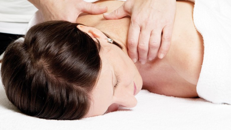 Massage, © VitalZeit Hotel Weber Eine Frau erhält eine Nackenmassage auf einem weißen Handtuch liegend.