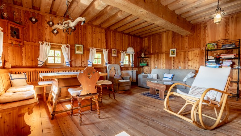 Essbereich, © Wiener Alpen / Christian Kremsl Essbereich mit Holzmöbeln, Schaukelstuhl und Sofa in einem Raum mit Holzvertäfelung.