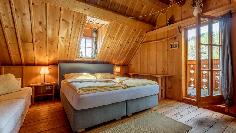 Kronaushof, © Wiener Alpen / Christian Kremsl Schlafzimmer mit Holzvertäfelung, Doppelbett, Teppich und offener Tür zum Balkon.