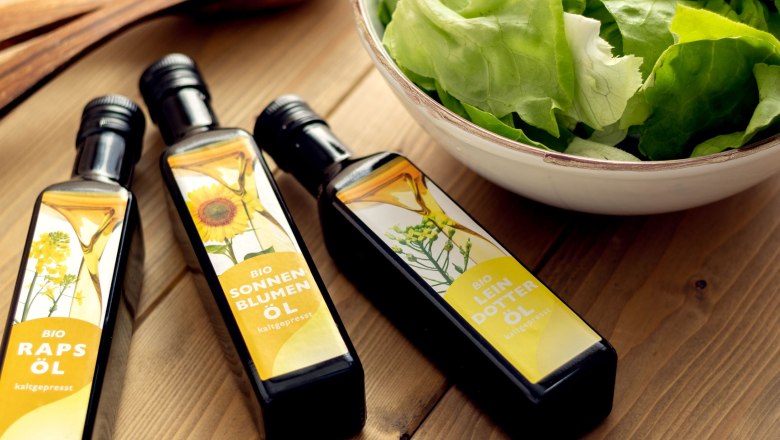 Öle, © Sooo gut schmeckt die Bucklige Welt/Viktoria Kornfeld Drei verschiedene Öle liegen auf einem Holztisch neben einer Schüssel mit grünem Salat.