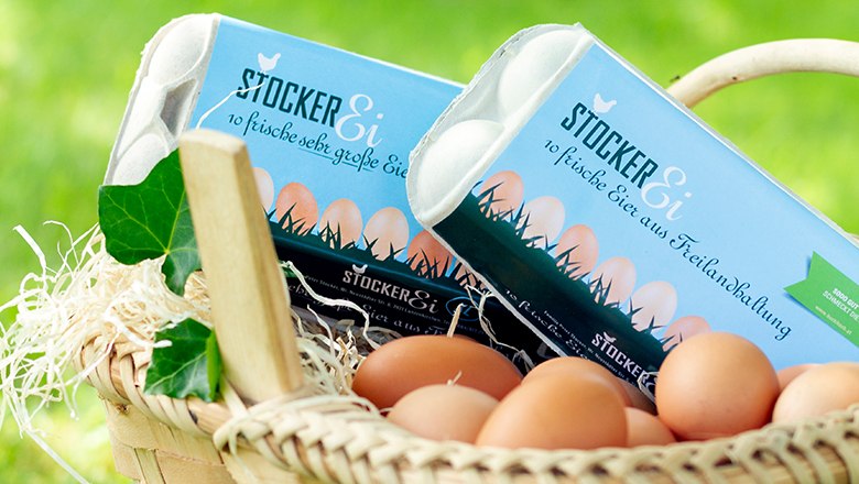 Stocker Ei, © Sooo gut schmeckt die Bucklige Welt/Viktoria Kornfeld Ein Korb mit zwei Eierkartons, Eiern, Stroh und Blättern vor einem grünen Hintergrund.