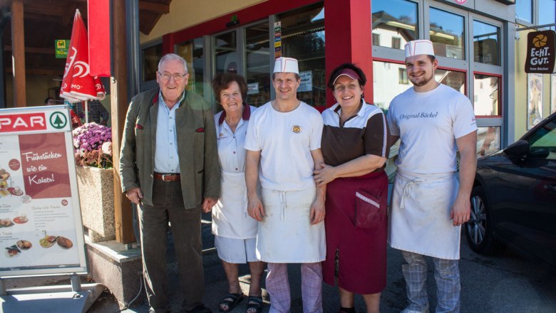 Familie Bernhard & Birnbauer, © Clemens Trenker, BA Fünf Personen stehen lächelnd vor einem Geschäftseingang.