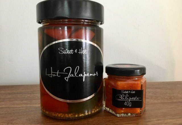 Sweet & Hot, © Böhm Ein Glas mit Jalapeños und ein kleines Glas mit Chilipaste auf einem Holztisch.