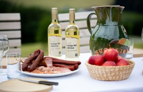 Genuss in der Buckligen Welt, © Wiener Alpen/Nicole Oberhofer Tisch mit Apfelmost, Wurstplatte, Äpfeln, Holzbrett, Messer und Gläsern.