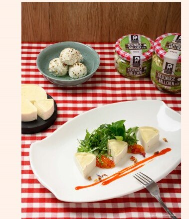 Ziegenfrischkäseterrine, © VitalZeit Hotel Weber Teller mit Ziegenfrischkäseterrine auf kariertem Tischtuch, daneben Ziegenkäsebällchen.