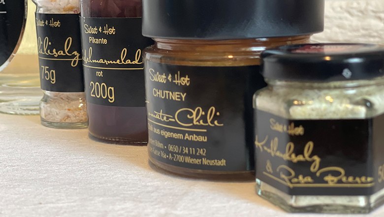 Chutneys, © Sooo gut schmeckt die Bucklige Welt Nahaufnahme von Gläsern mit Salz, Chutney und Marmelade mit schwarzem Etikett und goldener Schrift.