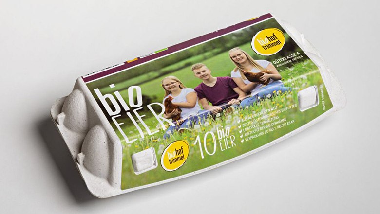 Eierkarton mit Bio-Eiern und einem Bild von drei Personen und Hühnern auf einer grünen Wiese., © Biohof Trimmel Eierkarton mit Bio-Eiern und einem Bild von drei Personen und Hühnern auf einer grünen Wiese.