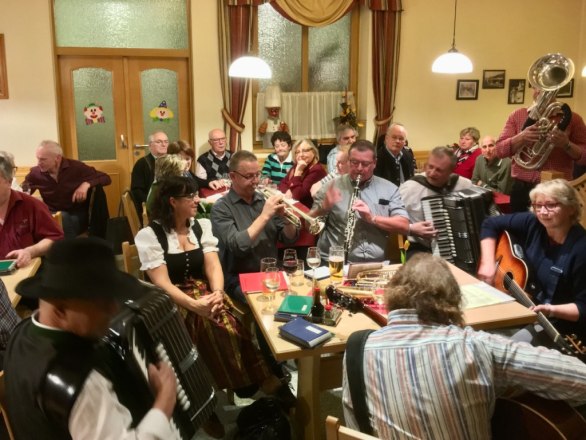 Menschen musizieren gemeinsam in einem Raum mit Instrumenten wie Akkordeon, Trompete und Gitarre.