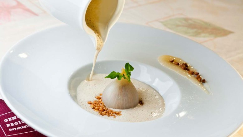 Gourmetgericht mit Zwiebel und Schaumsoße auf einem weißen Teller.
