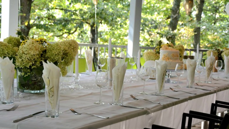 Feierlich gedeckter Tisch in weiß auf einer Terasse mit Blumen und Kerzen.