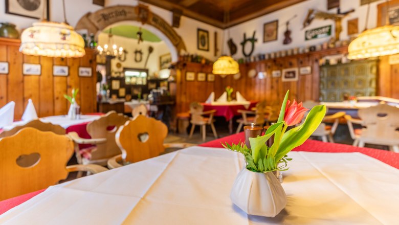 Gemütliches Gastzimmer mit Holzmöbeln, Tischdecken und Blumenvasen.