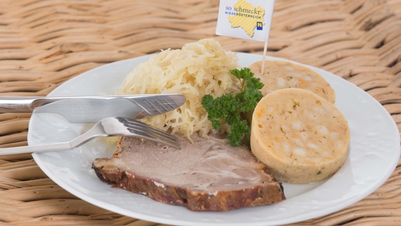 Wei&szlig;er Teller auf einem Korbtisch mit Schweinebraten, Kn&ouml;deln und Sauerkraut, garniert mit Petersilie.