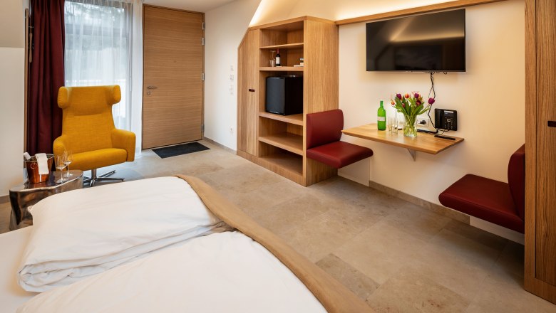 Modern eingerichtetes Hotelzimmer mit gelbem Sessel, Holzmöbeln und Blumen auf einem Tisch.
