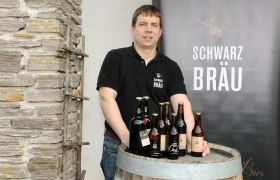 Ein Mann steht hinter einem Holzfass mit Bierflaschen der Marke Schwarzbräu.