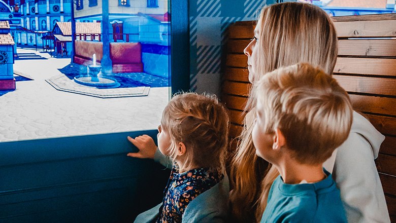 Zwei Kinder und eine Frau schauen aus dem Fenster eines Zuges auf eine virtuelle Stadt.