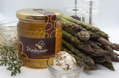 Ein Honigglas, Gläser mit Ziegenkäse, Spargel, Salz- und Pfefferstreuer vor weißem Hintergrund.