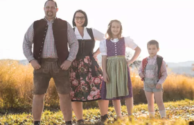 Eine Familie mit zwei Kindern in Tracht gekleidet steht auf einem Weg vor einem Feld.