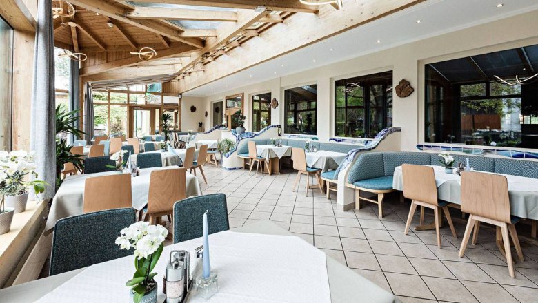 Ein heller Wintergarten mit gedeckten Tischen und Holzm&ouml;beln.