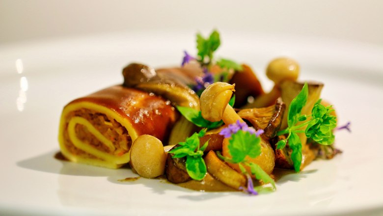 Gourmetgericht mit Pilzen und frischen Kräutern auf weißem Teller angerichtet.