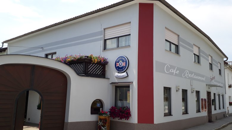 Außenansicht Café Sabine mit Holztor, weiß-roter Fassade und Aufschrift "Café-Restaurant".