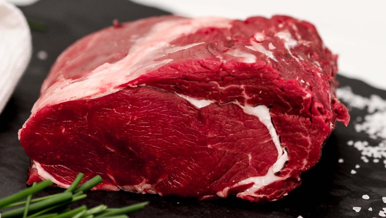 Ein rohes Stück Rindfleisch liegt auf einer dunklen Schieferplatte neben Salz und Schnittlauch.