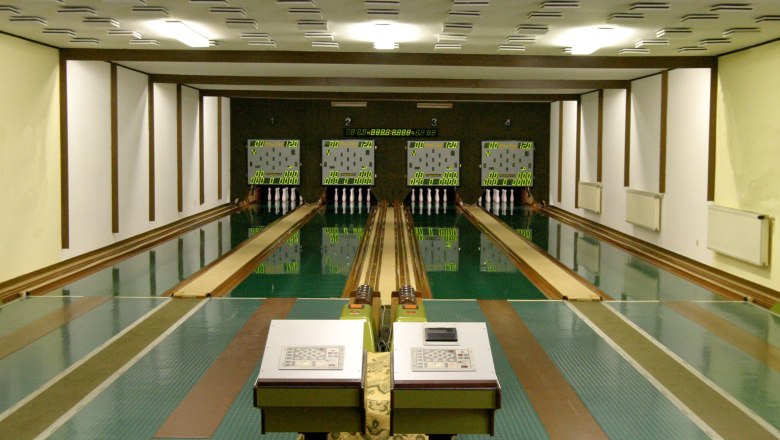 Innenansicht einer Kegelbahn mit vier Bahnen und Anzeigetafeln.