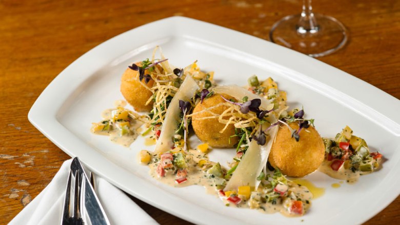 Drei goldbraune Kroketten auf einem weißen Teller, garniert mit Gemüse und Sauce.
