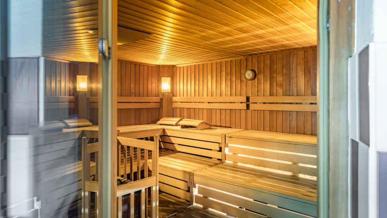 Innenansicht einer leeren Sauna mit Holzbänken und Wanduhr.