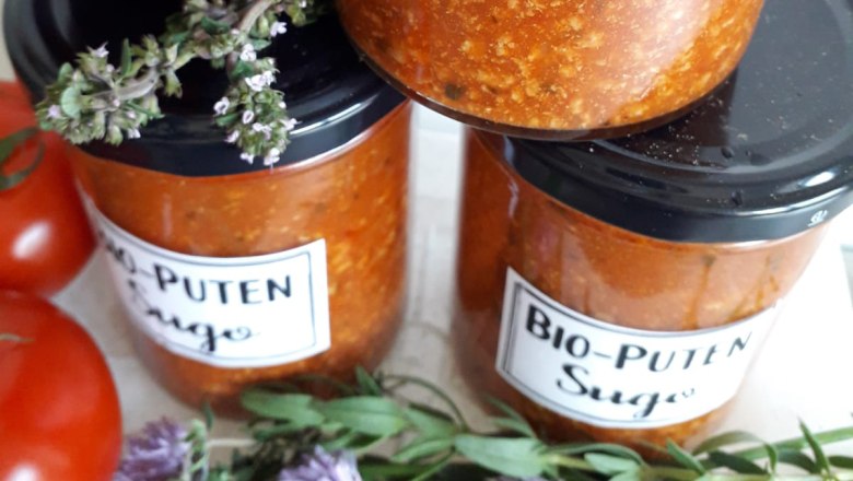 Gläser mit Bio-Puten Sugo, daneben Tomaten und Kräuter.