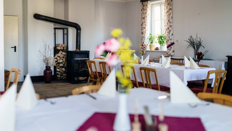 Gemütlicher Gastraum mit Holzofen, gedeckten Tischen und Blumen.