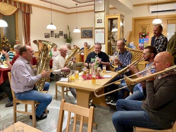 Gruppe von Männern spielt Blasinstrumente in einer gemütlichen Gaststube.