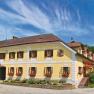 Traditionelles Gasthaus mit gelber Fassade, umgeben von grüner Landschaft und blauem Himmel.