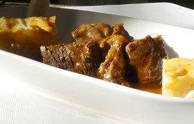 Tiefer, weißer Teller mit geschmortem Wildschweinbraten und Beilagen.