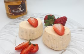 Zwei geeiste Honigherzen auf Glasteller, ganiert mit Erdbeeren. Im Hintergrund ein Honigglas.