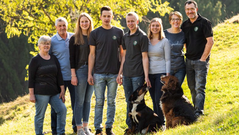 Eine große Familie mit zwei Hunden steht auf einer grünen Wiese vor einem Baum.
