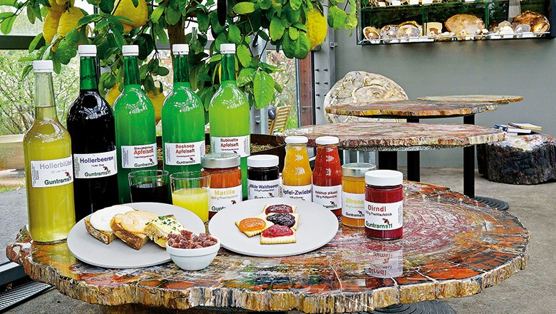 Verschiedene Flaschen und Gläser mit Getränken und Marmeladen auf einem Tisch aus versteinertem Holz.