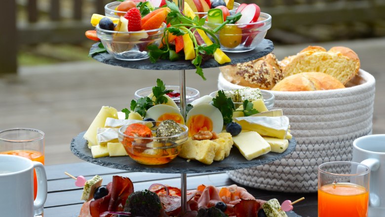 Etagere mit Aufschnitten, Käse und Gemüse, daneben Getränke und ein Brotkorb.