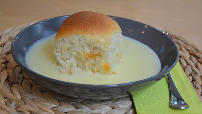 Ein schwarzes Teller mit einer Buchtel und Vanillesoße, daneben grüne Serviette mit Gabel.