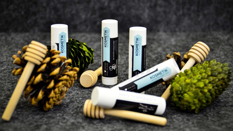 Lippenbalsam mit Tannenzapfen und Höniglöffeln auf dunkelgrauem Hintergrund.