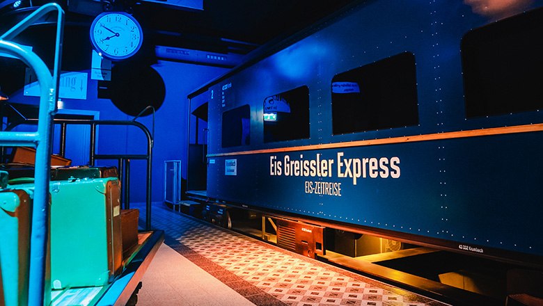 Ein Waggon der Eis-Zeitreise in einem abgedunkelten Raum, daneben ein Gepäckwagen.
