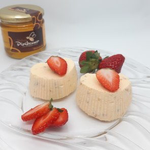 Zwei geeiste Honigherzen auf Glasteller, ganiert mit Erdbeeren. Im Hintergrund ein Honigglas.