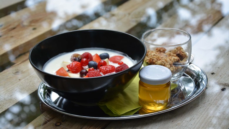 Schwarze Schale mit Joghurt und Beeren auf silbernen Tablett mit Honig und Müsli.